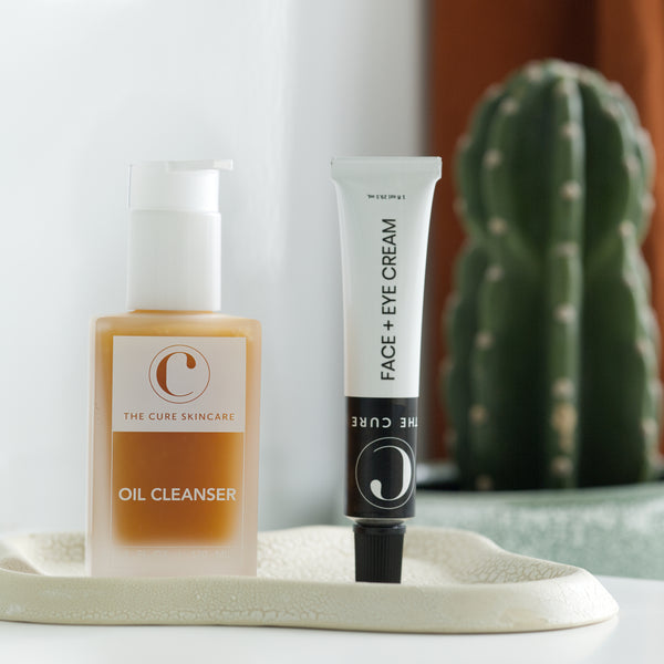 Two skincare products, 'Oil Cleanser' and 'Face + Eye Cream', on a tray with a cactus in the background.